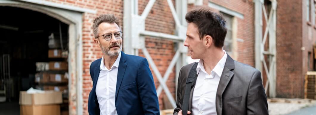 Two businessmen walking and talking at an old brick building