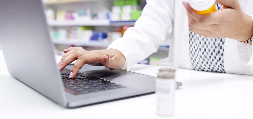 Hands of chemist in a pharmacy checking medicine on a laptop at a dispensary. Closeup of a pharmacist filling a prescription, or checking information online for medication inside a drugstore