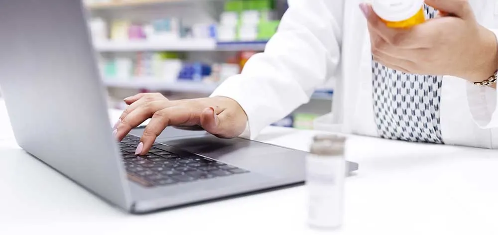 Hands of chemist in a pharmacy checking medicine on a laptop at a dispensary. Closeup of a pharmacist filling a prescription, or checking information online for medication inside a drugstore
